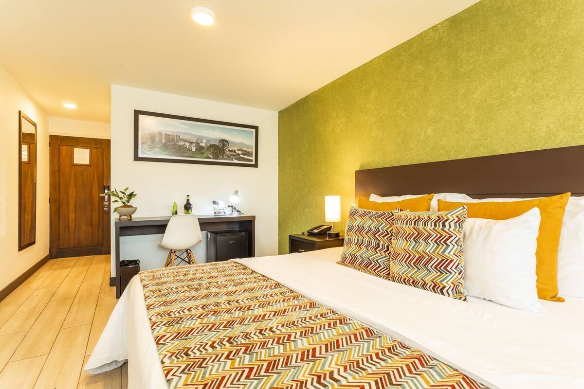 Una habitación de hotel con cama, escritorio, silla y un cuadro en la pared.
