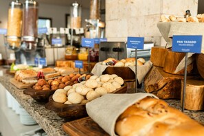 Un bufé con panes y pasteles variados, incluyendo un letrero que dice 'Pandedro' y 'Pan Tajo'.