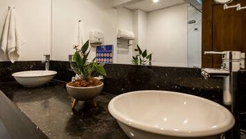 A bathroom with a large freestanding bathtub, a sink with a bowl, a mirror, a towel rack, and a potted plant.