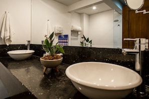 A bathroom with a large freestanding bathtub, a sink with a bowl, a mirror, a towel rack, and a potted plant.