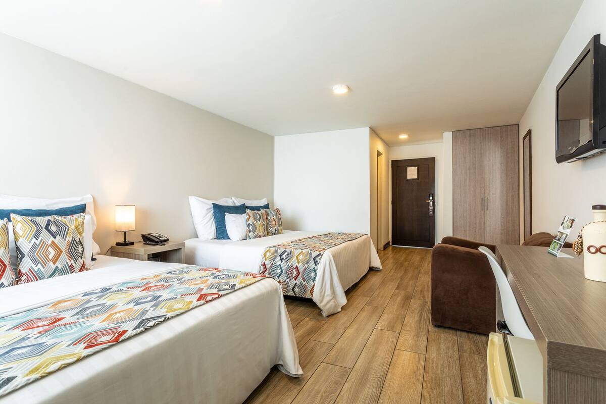A hotel room with two beds, a desk, a chair, and a TV.