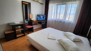 Quarto de hotel com uma cama, uma escrivaninha com cadeira, televisão e uma janela com cortinas.