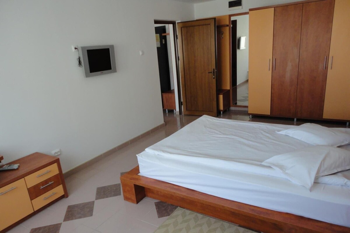 A bedroom with a bed, wooden wardrobe, and a television mounted on the wall.