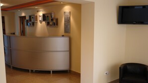 A reception area with a reception desk, a black leather chair, and a mounted television. - Hotel Arion (Constanta)