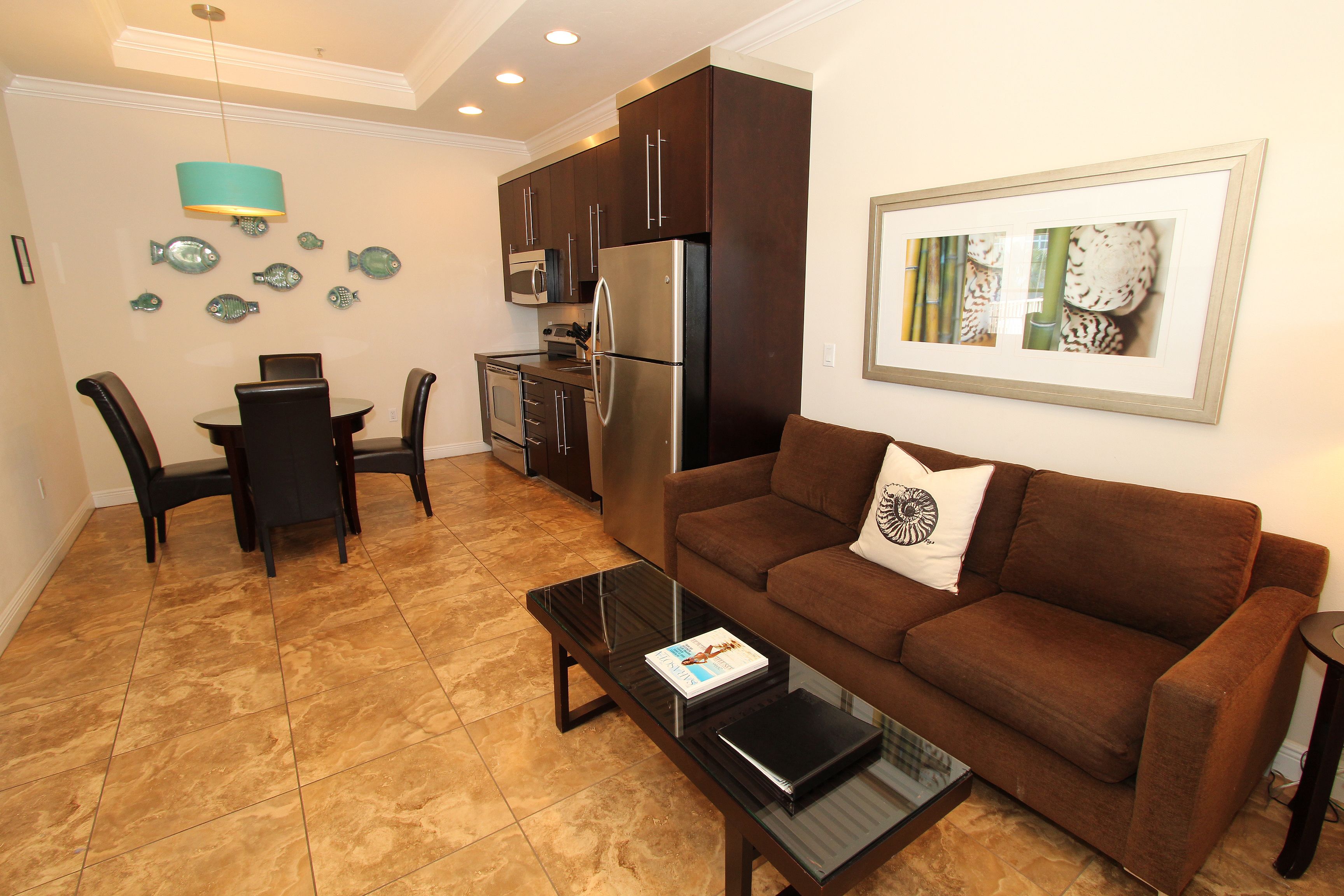 A compact living space with a brown sofa, a dining table with chairs, a kitchen area with dark cabinets, and a framed picture on the wall.