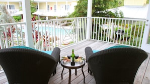 A wooden deck with two wicker chairs and a small table set for two, overlooking a pool and a garden.
