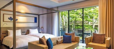 Habitación de hotel con cama con dosel, sofá, mesa de centro y balcón con mobiliario exterior.
