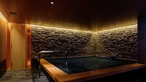 Un hidromasaje con paredes de piedra, un banco de madera, una puerta de madera y suelo de piedra.