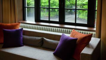A sofa with cushions, a radiator, and a window with a view of greenery.