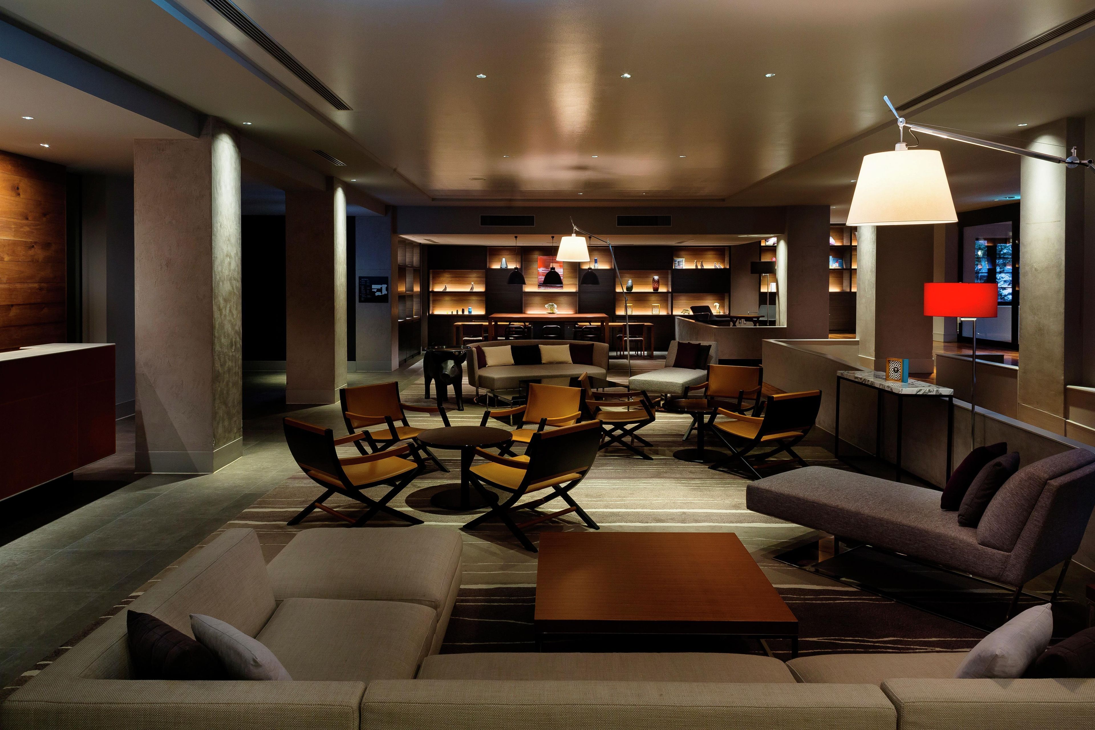 A modern hotel lobby with a seating area, a bar, and a dining space.