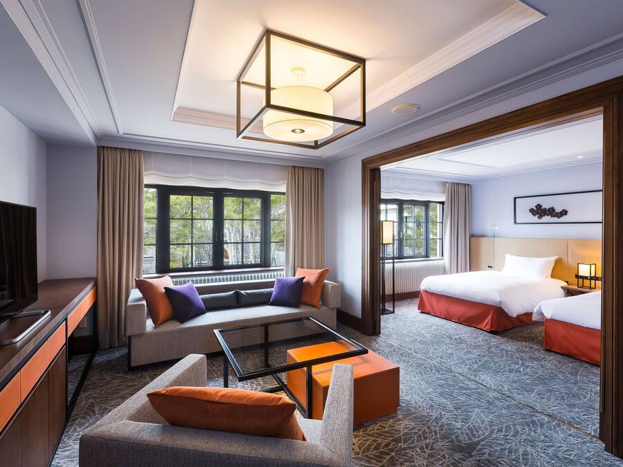 A hotel room with a sofa, a bed, a TV, and a large window.