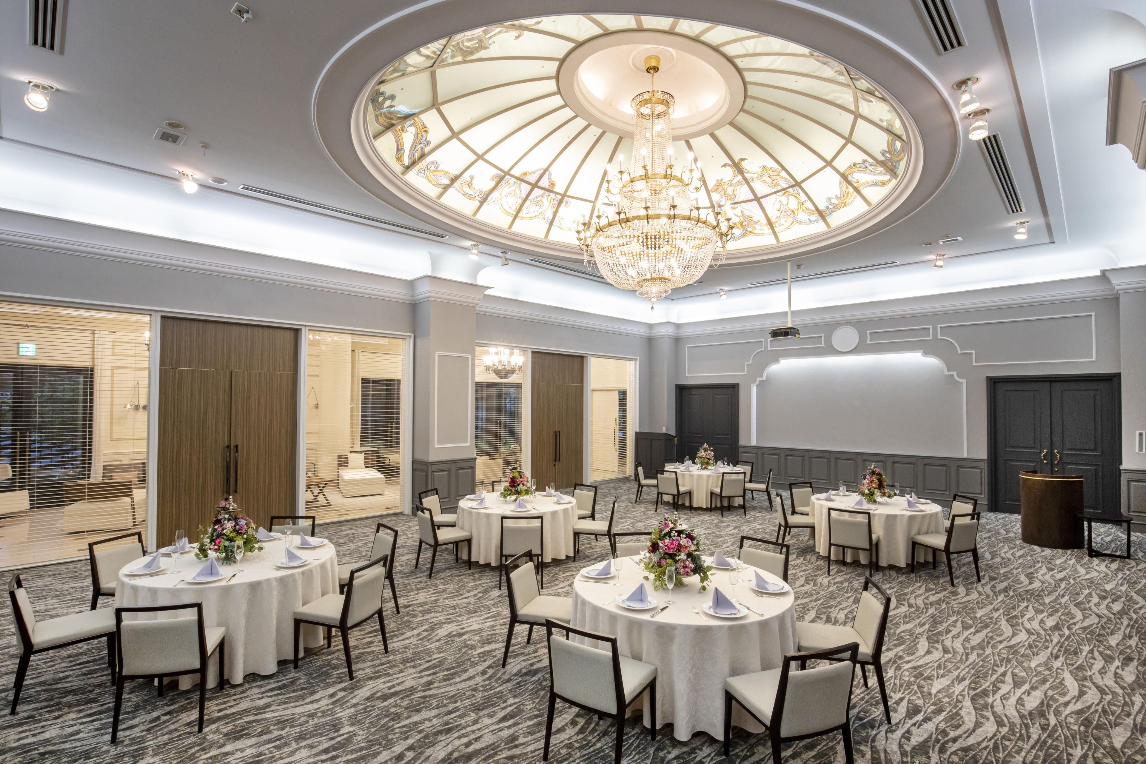 Un salón de conferencias de hotel con varias mesas redondas, manteles blancos y sillas.