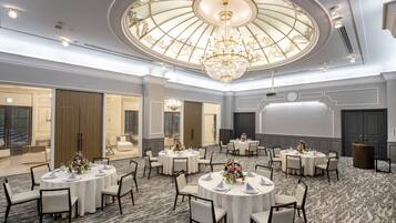 Un salón de conferencias de hotel con varias mesas redondas, manteles blancos y sillas.