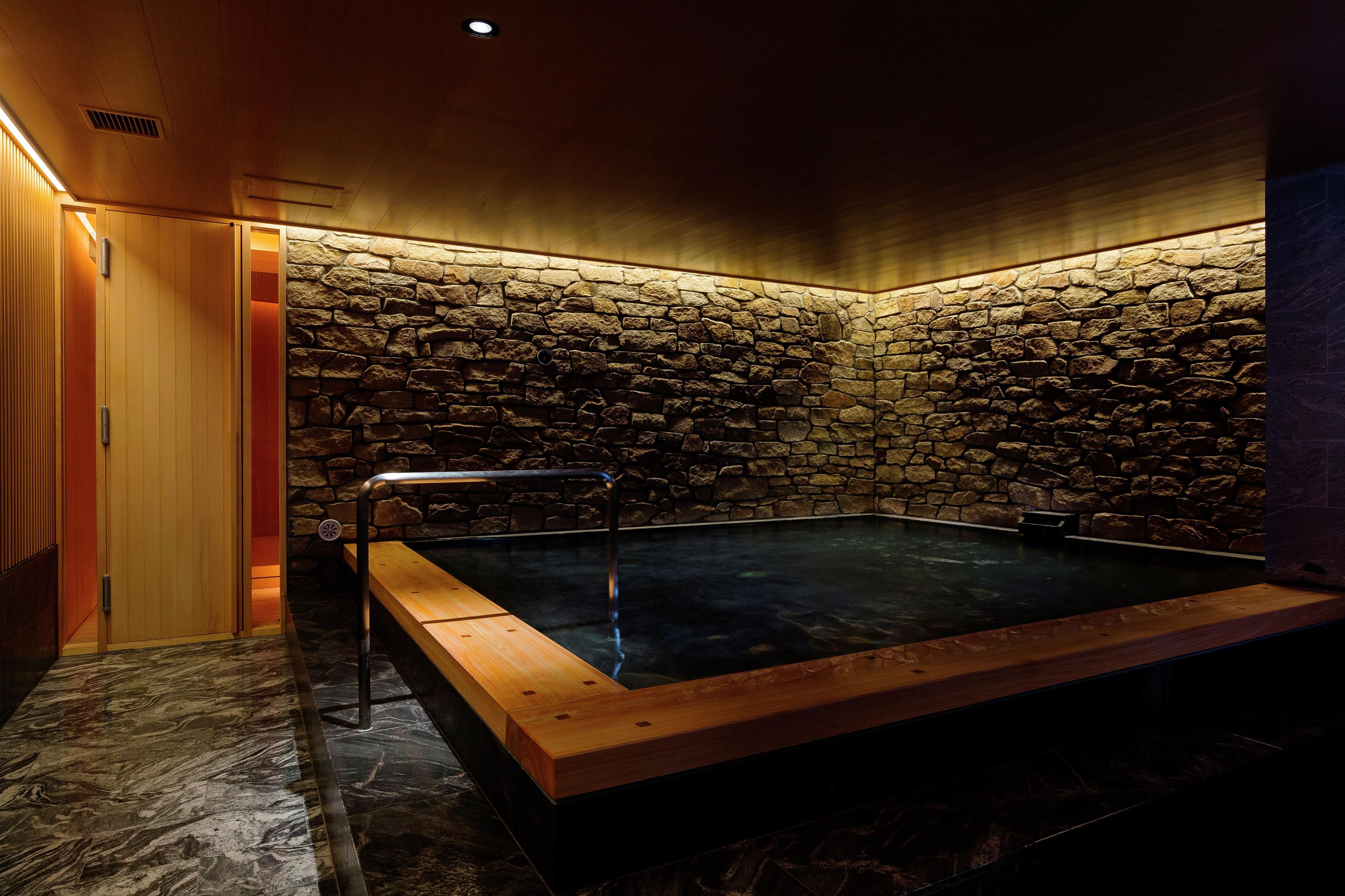 A spa room with a stone wall, a wooden bench, and a hot tub.