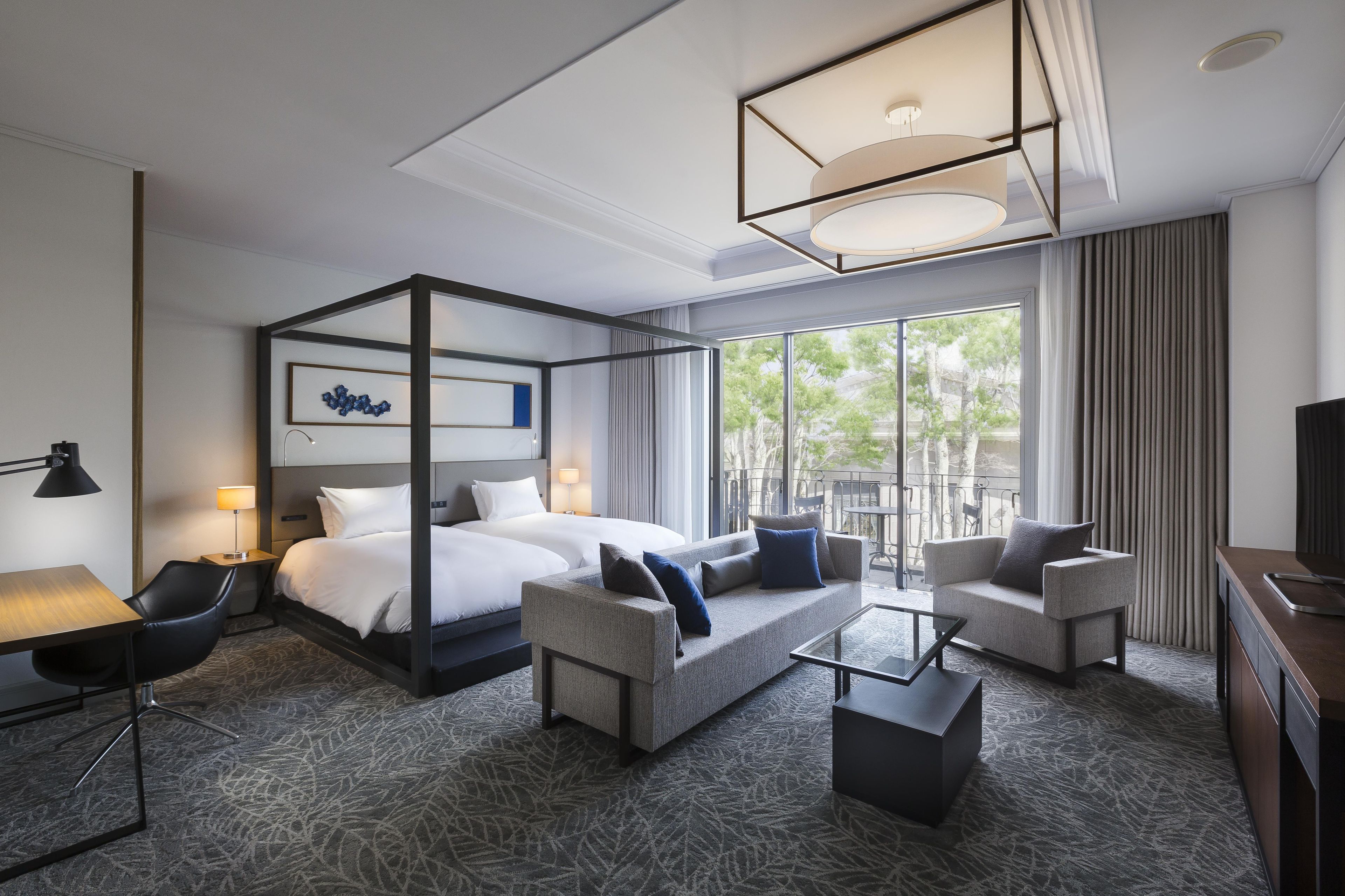 A hotel room with a four-poster bed, a sofa, a coffee table, and a TV.