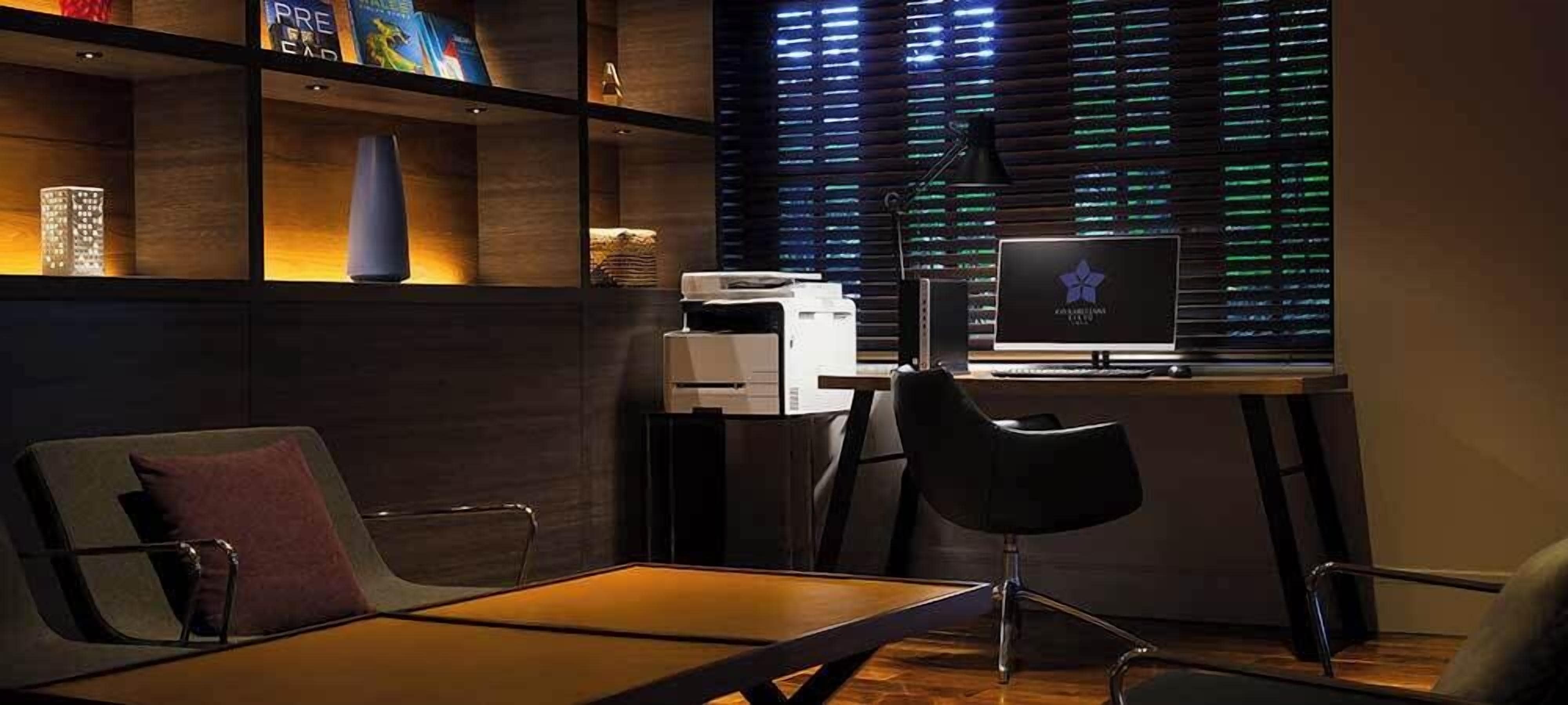 A modern office with a desk, chairs, a computer, and a window with blinds.