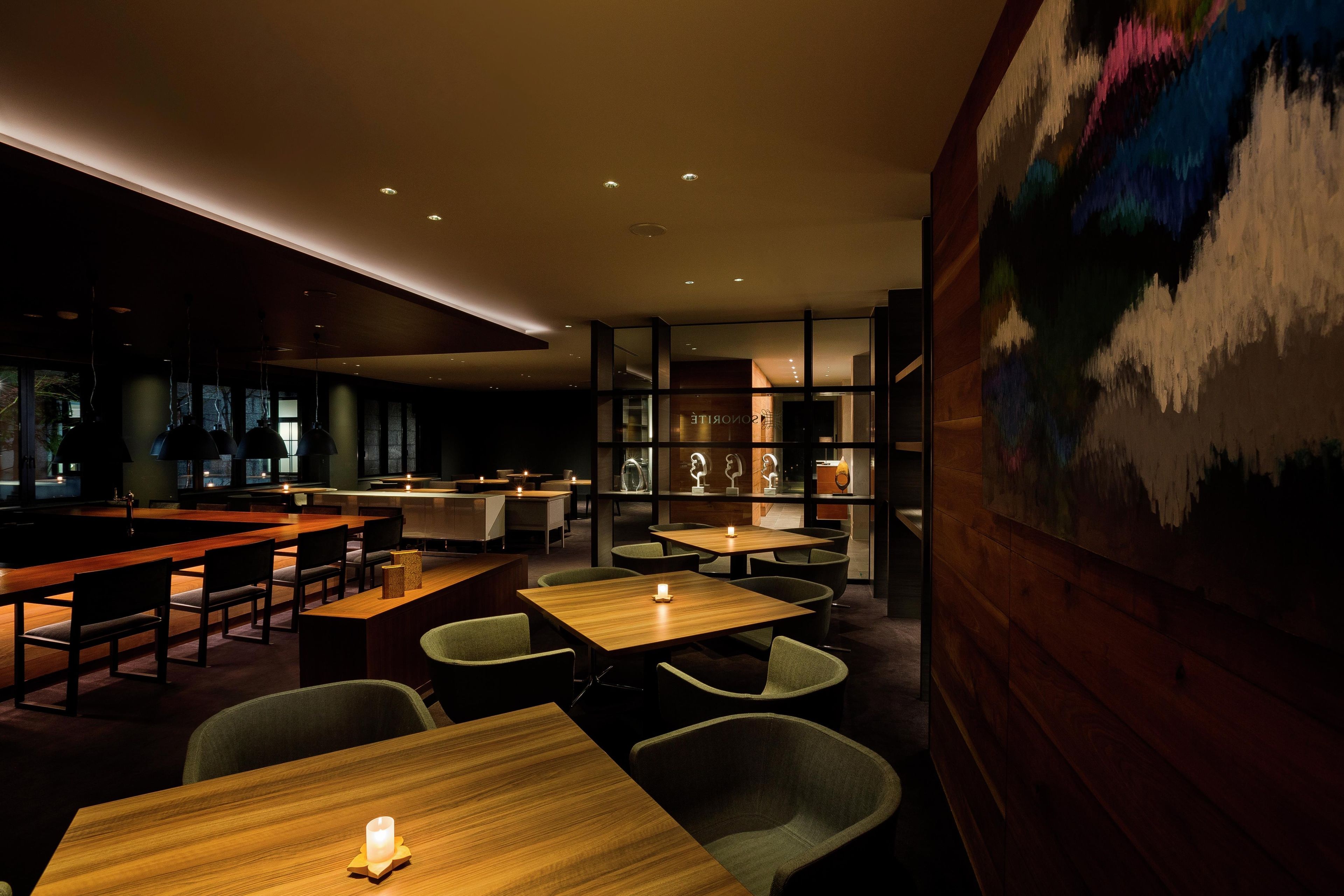 A modern interior with wooden tables and chairs, a bar area, and a large abstract painting on the wall.