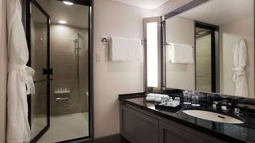 A modern bathroom with a glass-enclosed shower, a large mirror, and a black countertop with a sink and toiletries.