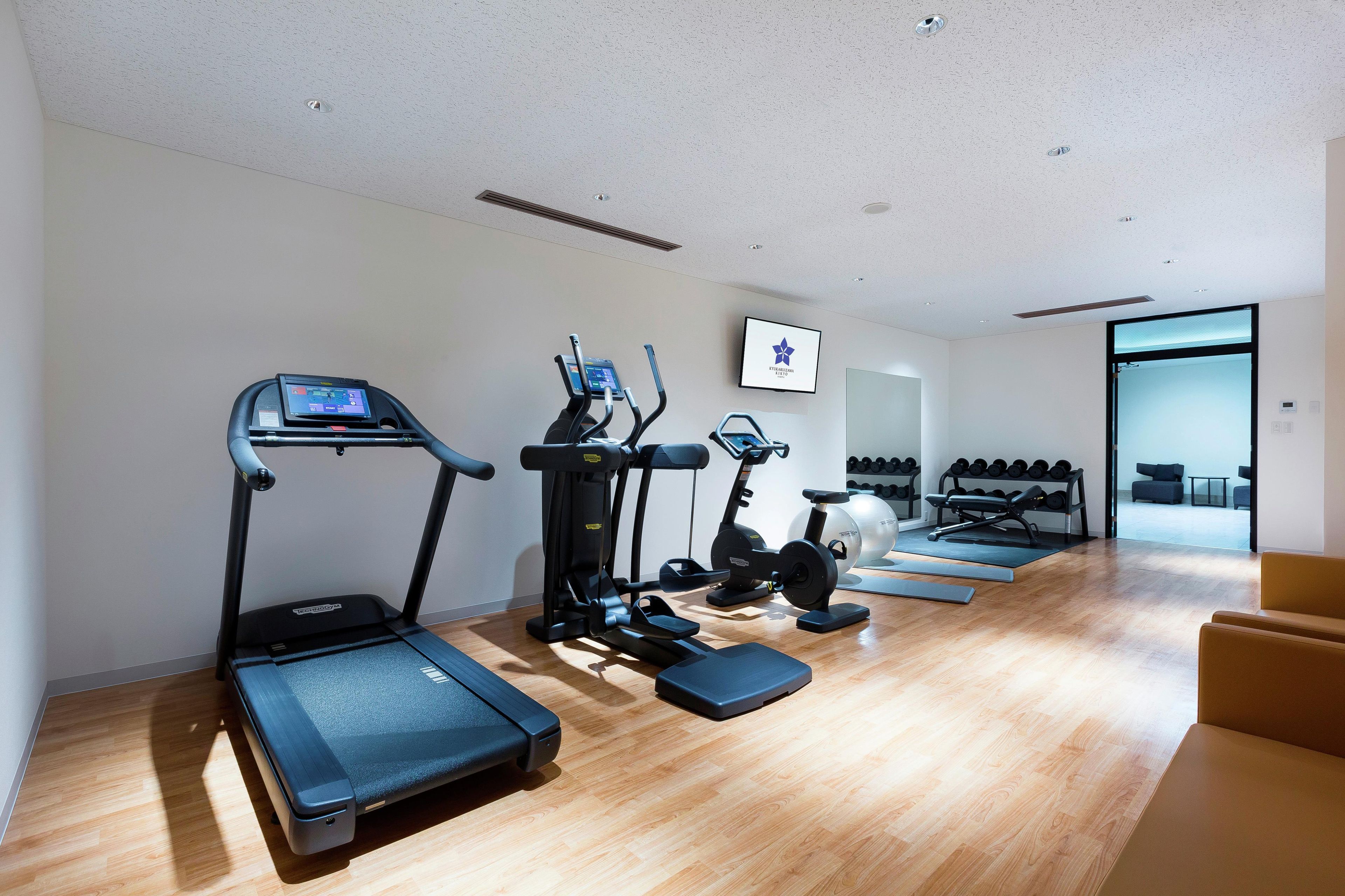 Ein Fitnessraum mit Laufbändern, Crosstrainern und einer Gewichtbank.