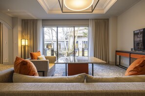 Habitación de hotel con sofá, una mesa de centro de vidrio, televisor y vistas al exterior.