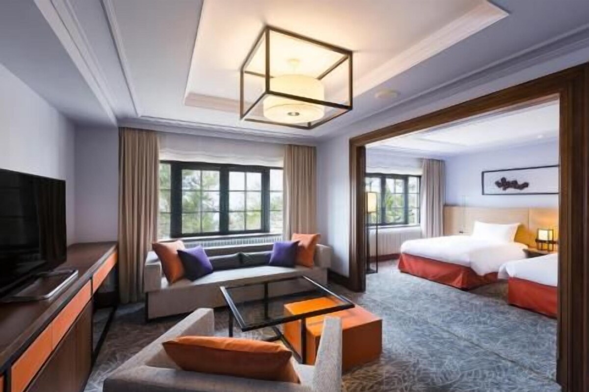 A hotel room with a sofa, a TV, a bed, and a large window.
