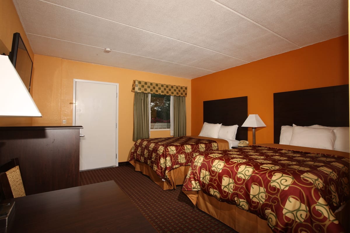 Une chambre d’hôtel avec deux lits, un bureau, une chaise, une porte et une fenêtre avec des rideaux.