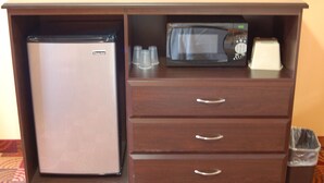 Una kitchenette compacta equipada con refrigerador, microondas y un basurero pequeño.