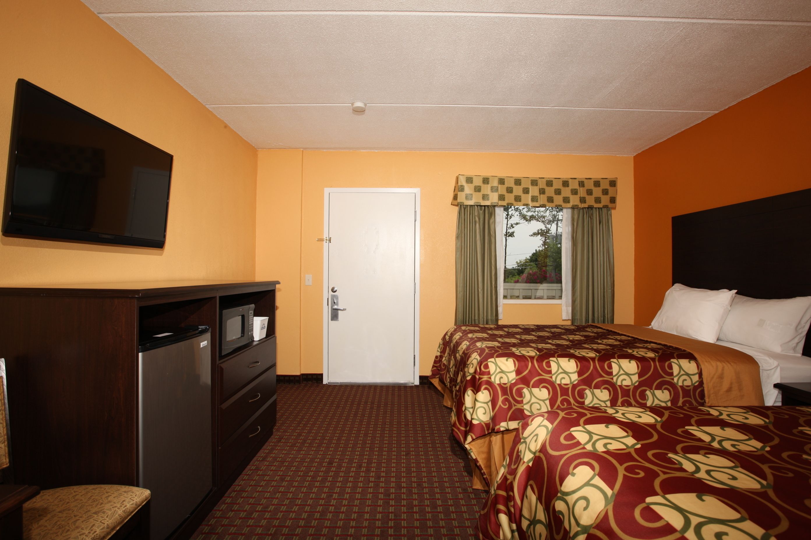 A hotel room with a bed, a TV mounted on the wall, a desk with a microwave, and a door.