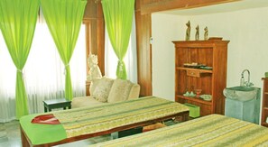 A room with a bed, a wooden cabinet, a small table, and a window with green curtains. - Dewani Villa Resort (Kerobokan)