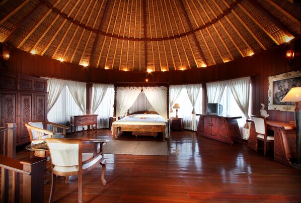 A spacious room with a large bed, wooden furniture, and a high ceiling with a thatched roof. - Dewani Villa Resort (Kerobokan)