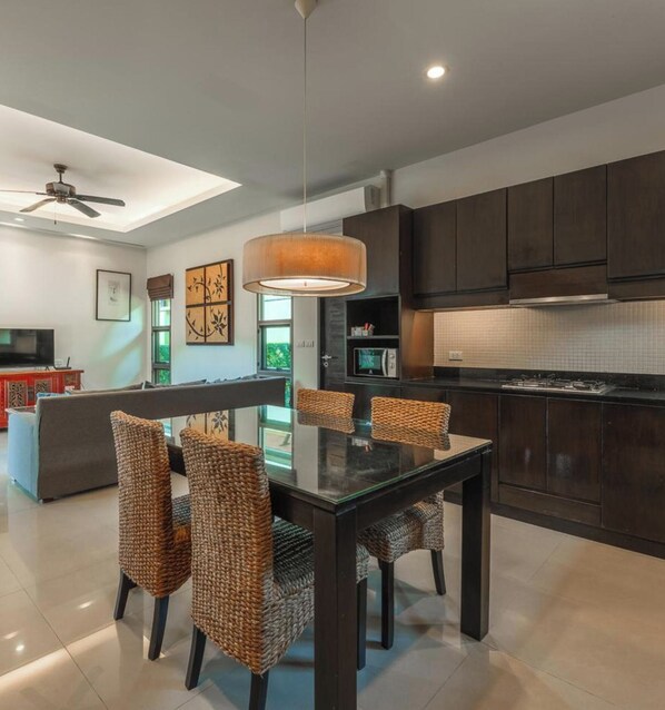 Una cocina moderna con muebles oscuros, una mesa de vidrio y sillas de mimbre.