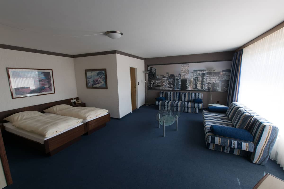 A hotel room with a bed, a sofa, a small table, and a cityscape view through the window.