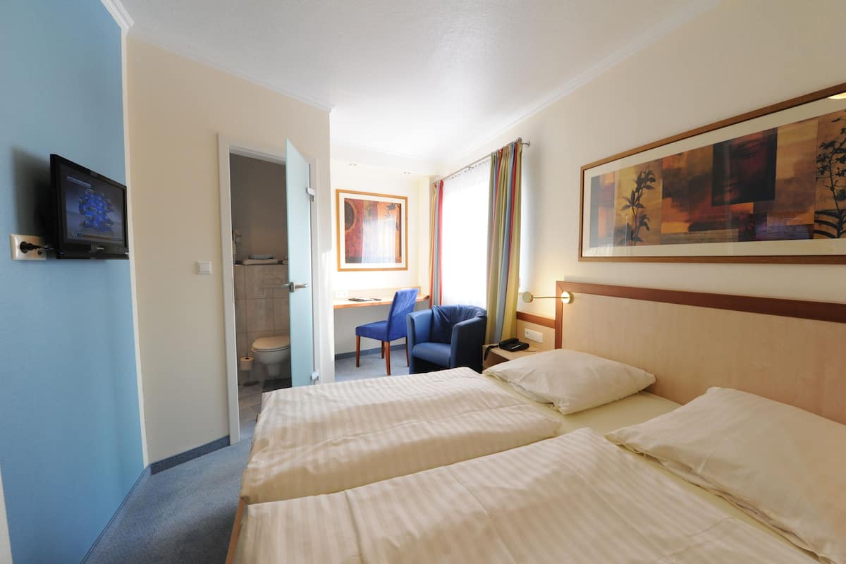 A hotel room with two beds, a desk with a chair, a television, and a painting on the wall.