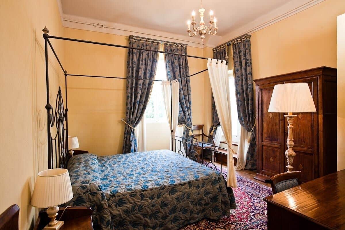 A bedroom with a four-poster bed, a wooden desk, a chair, and a chandelier.