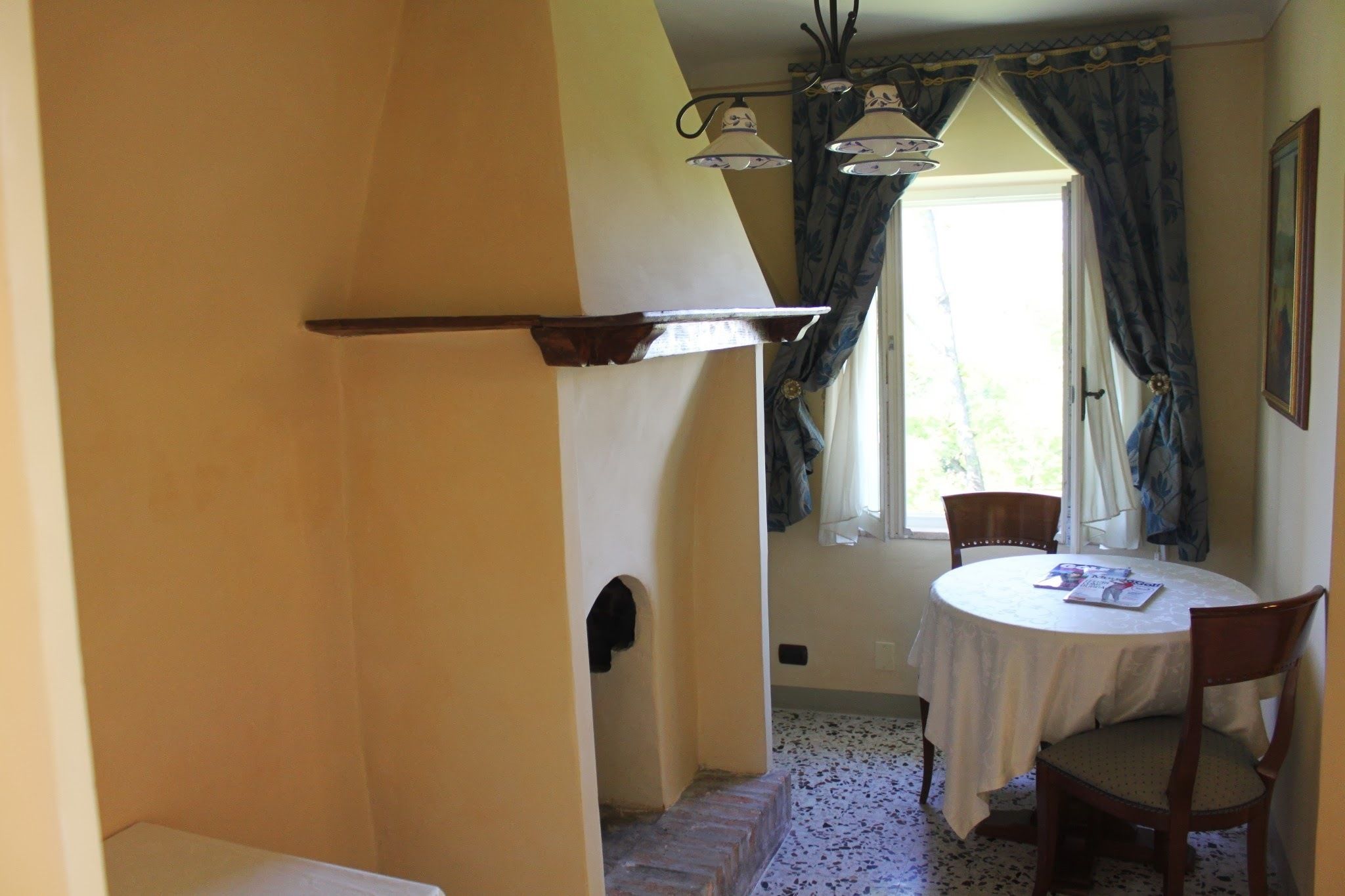 A dining area with a round table, chairs, a white tablecloth, and a window with curtains.