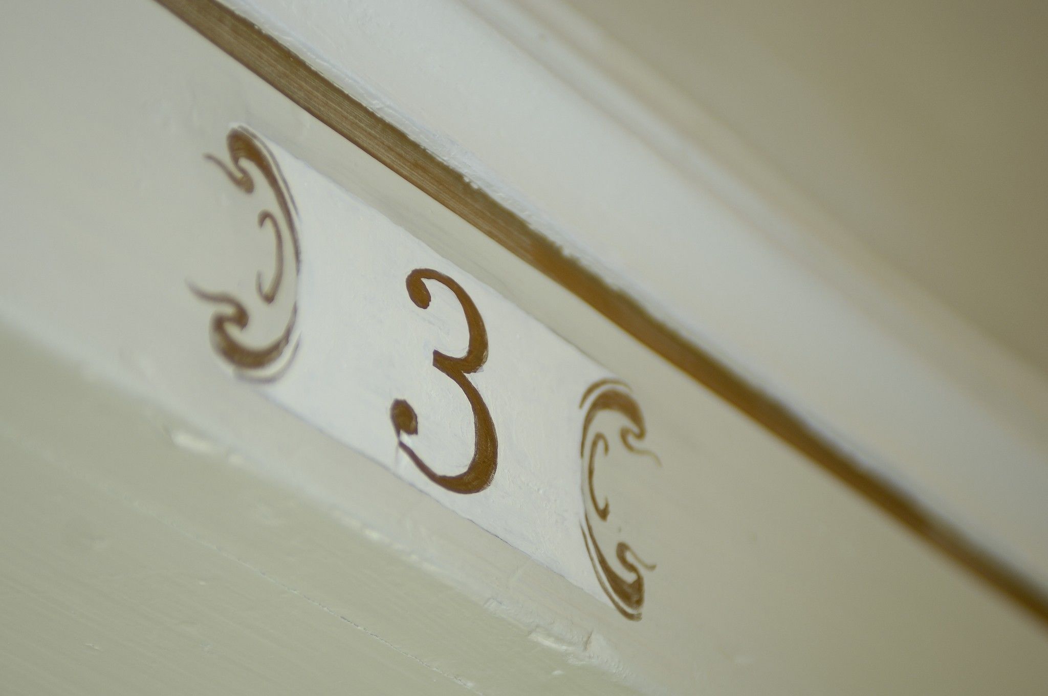 A close-up of a white wall with the number "3" and decorative swirls.