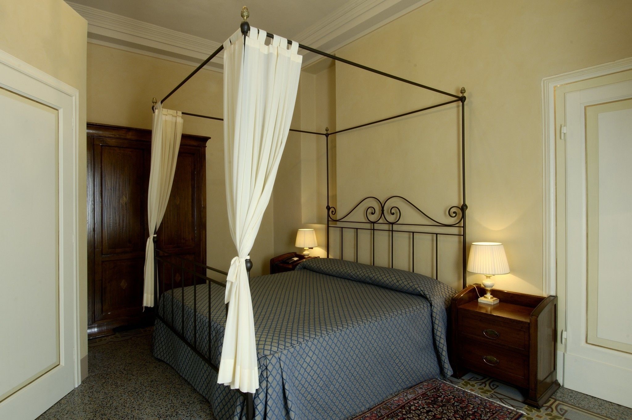 A four-poster bed with a canopy, a bedside table with a lamp, and a wooden wardrobe.