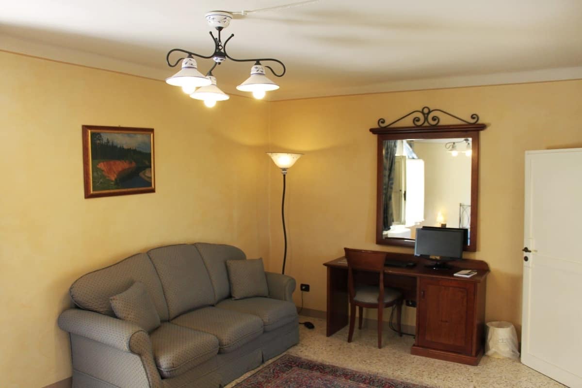 A room with a grey sofa, a desk with a computer, a mirror, and a painting on the wall.