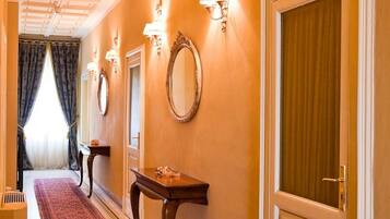 A hotel hallway with a red carpet, a wooden bench, a mirror, and a door with a curtain.