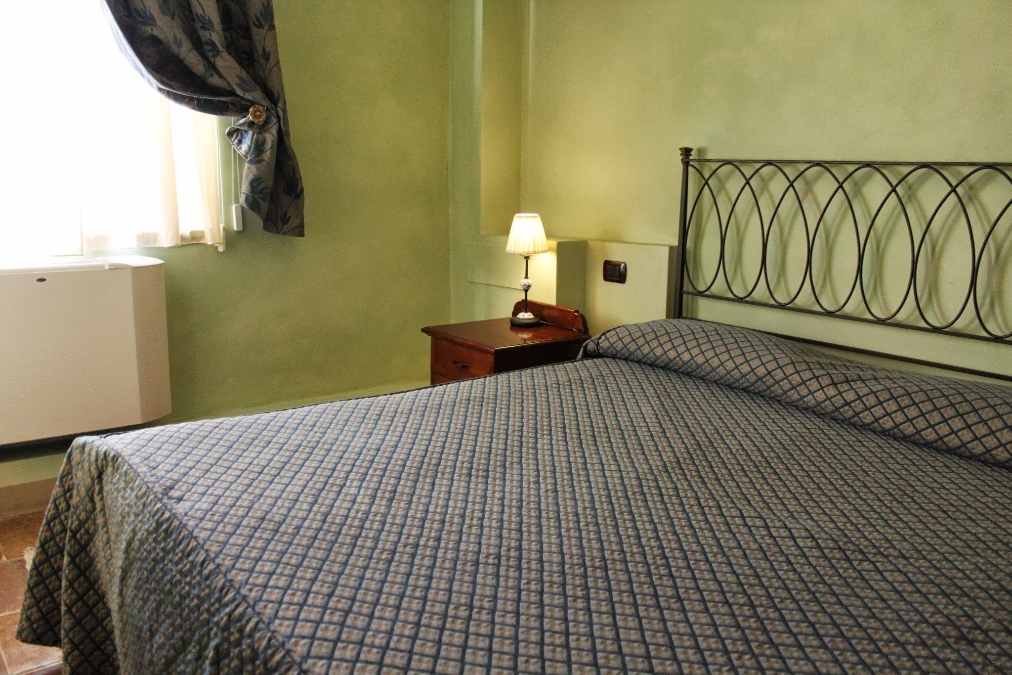 Ein Schlafzimmer mit einem Bett, einem Nachttisch mit Lampe und einem Fenster mit Vorhängen.