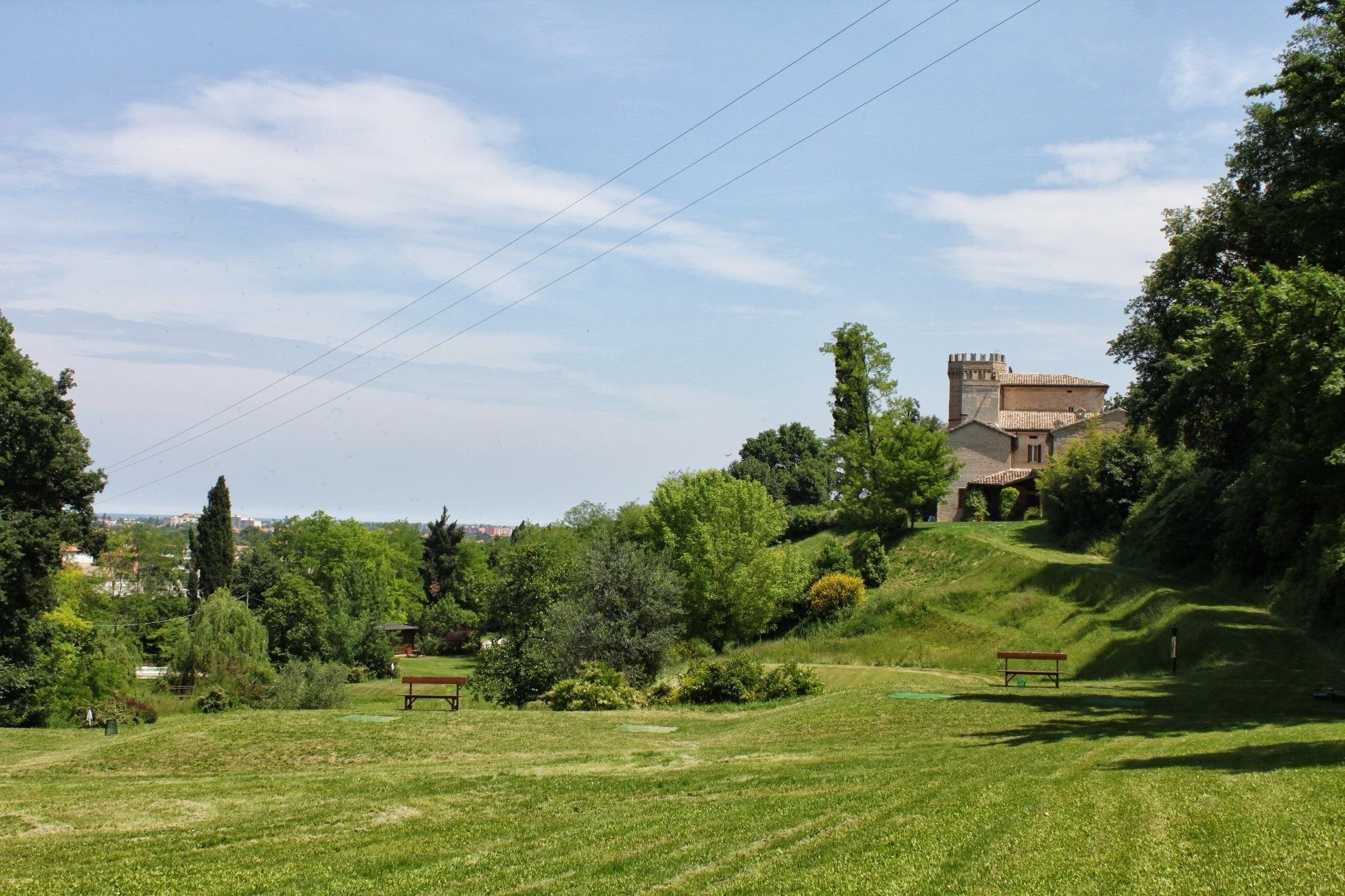 A grassy park with benches and a building with a tower.