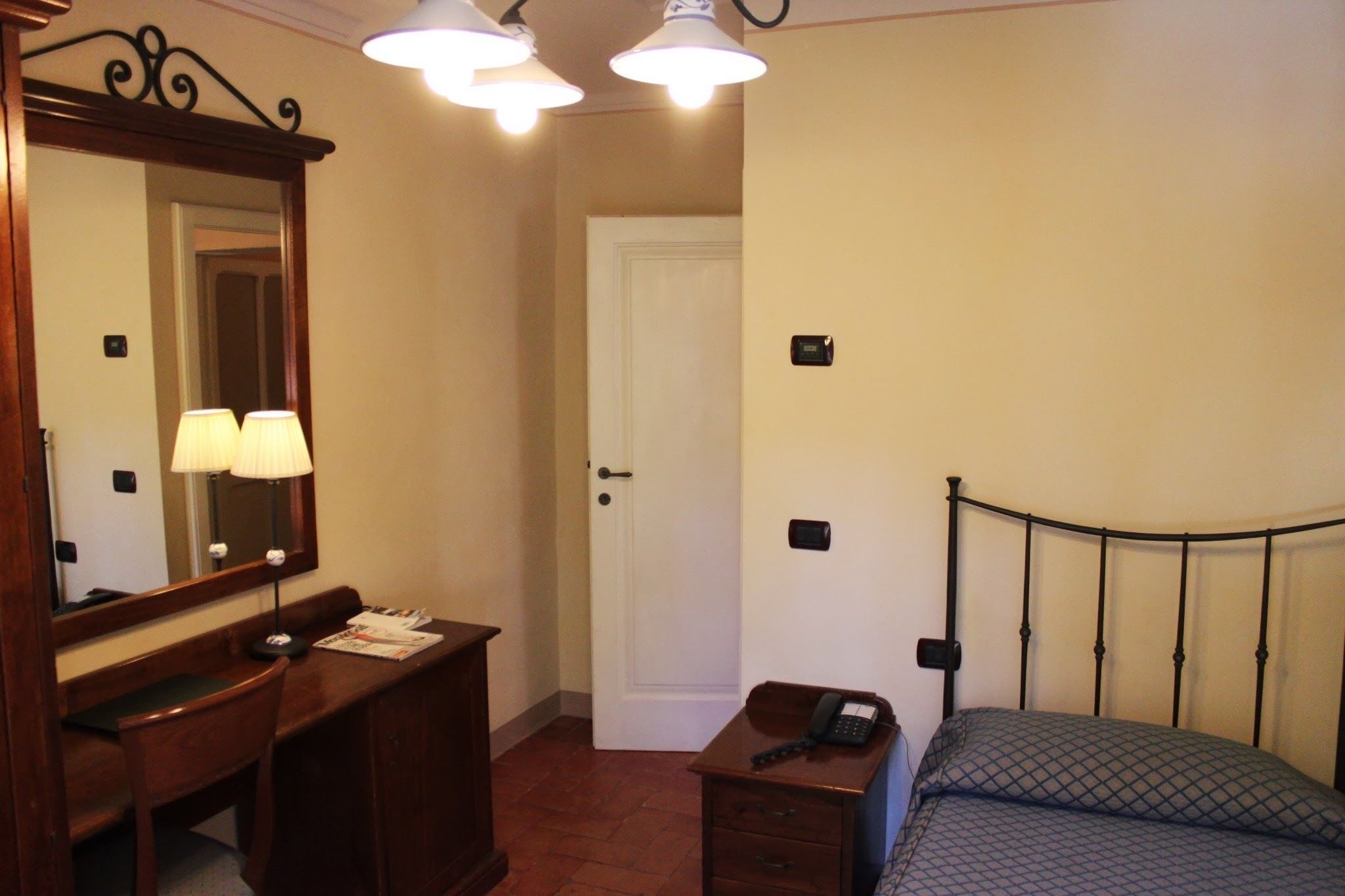 Une chambre d’hôtel avec un lit, un bureau avec une lampe, un miroir et une porte.