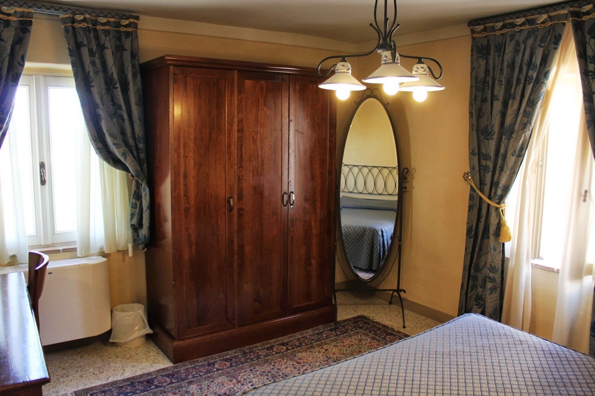 Een slaapkamer met een houten garderobe, een bed met een bedsprei met patroon, een grote spiegel en een radiator.