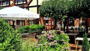 A courtyard with a pond, surrounded by lush greenery and a building with a distinctive fish logo. - Dom Oliwski (Gdansk)