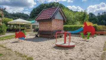 Ein Spielplatz mit einer Spielhaus aus Ziegeln, Schaukeln und einer Rutsche.