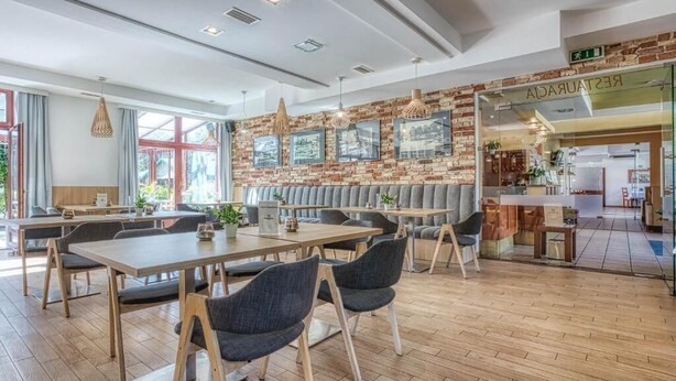 A modern restaurant with wooden tables and chairs, brick walls with framed pictures, and a visible restaurant sign. - Dom Oliwski (Gdansk)