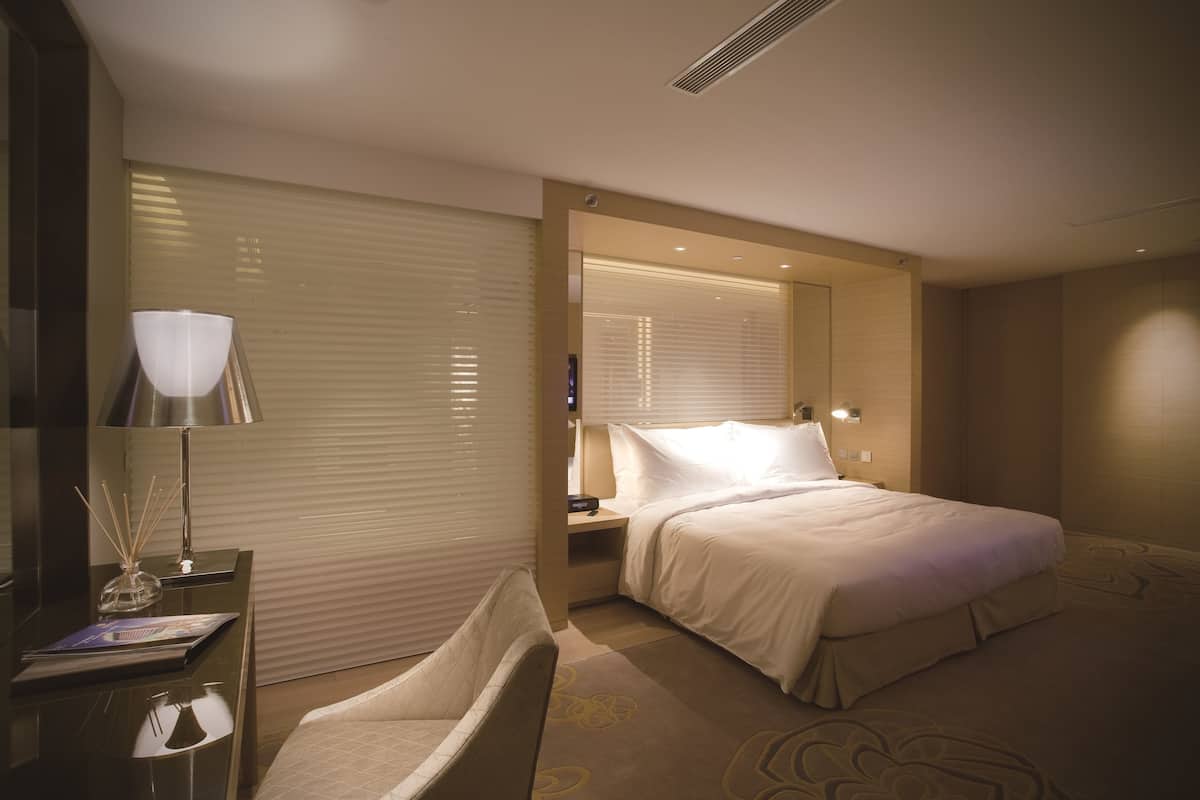 Una habitació d'hotel amb llit, taula de nit, làmpada i una cadira.