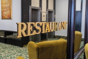 Placa com a palavra 'RESTAURANT' no hall, com carpete estampado e uma poltrona amarela.