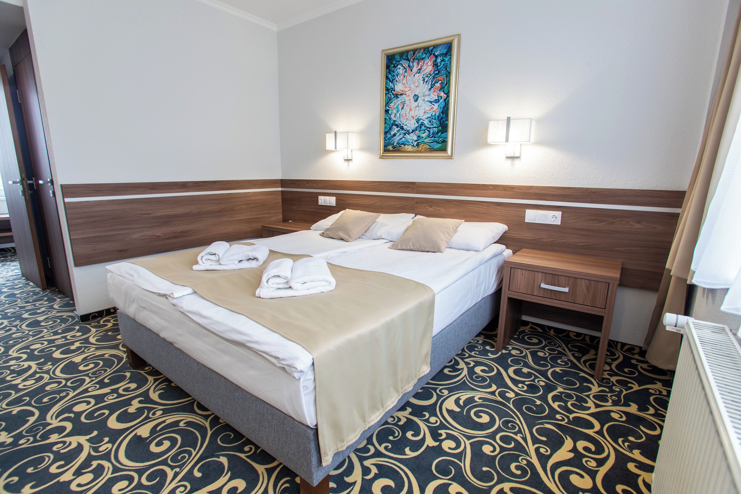 A hotel room with a large bed, bedside tables, a headboard, and a painting on the wall.