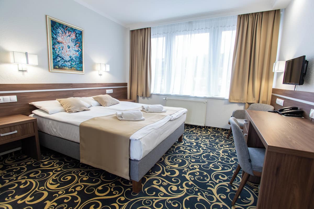 Ett hotellrum med en säng, ett skrivbord, en stol, en tv och en tavla på väggen.